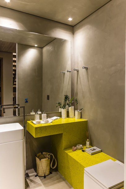 <span>Lavabo - Flávia Fernandes e Camila Carrasco. Na “caixa de concreto”, destacam-se a bancada em quartzo amarelo, a linha de objetos de porcelana desenhada especialmente para o evento e a iluminação aconchegante.</span>