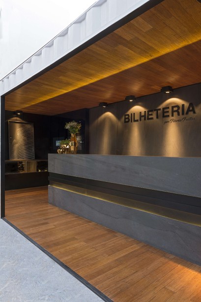 Bilheteria - Flávia Freitas. O espaço foi projetado em dois containers. O superior em balanço reserva o espaço da diretoria do evento. Utilizando madeira e porcelanato em cor de concreto, os tons escolhidos são em sua maioria neutros, criando uma caixa moderna e bastante acolhedora.