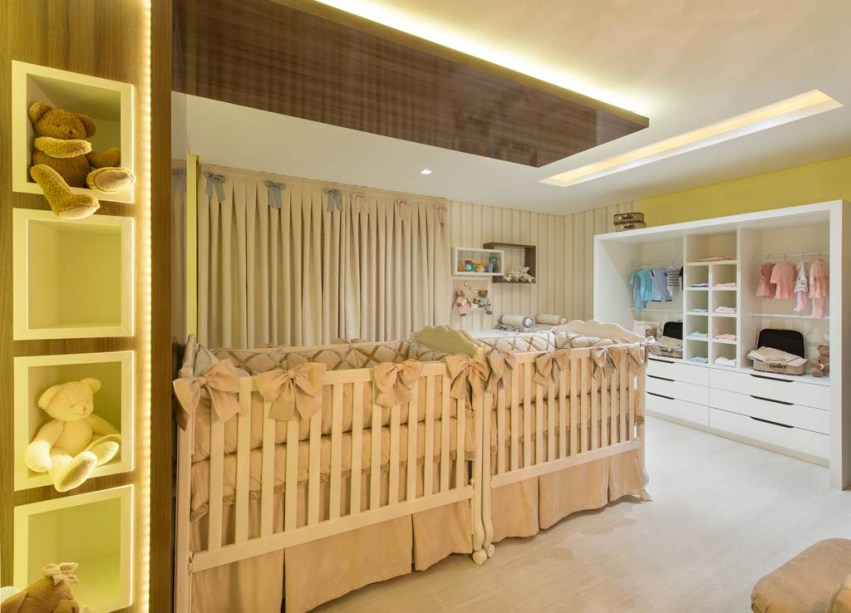 CASACOR Santa Catarina 2015 | Babies Room - Janete Krueger - O espaço de 25m² foi pensado para abrigar gêmeos e é otimizado com o mobiliário sob medida, executado em MDF. No teto, intercalam-se efeitos de iluminação, que vaza pelo recorte que demarca a área do armário aberto ou escapa pelas laterais da placa amadeirada acima dos berços. Essa placa abraça uma das paredes e envolve os nichos iluminados com LEDs. O piso vinílico clicado é antialérgico, térmico e fácil de limpar, o que é fundamental neste tipo de ambiente.