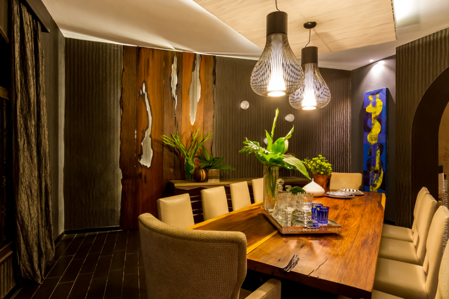 COMEDOR PRINCIPAL - GABRIELA FLORES E MAYA MAC LEAN. Eclético, o estilo da sala de jantar assume a elegância dos móveis laqueados e destaca o contraste com a madeira natural, trabalhada em conjunto com a Kirah Design. Teto e paredes são construídos em camadas, valorizadas pela iluminação. O azul profundo se impõe nos detalhes e conecta todas as áreas.