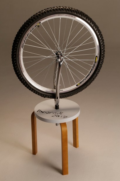 A proposta do artista plástico Marcelo Paciornik é fazer uma homenagem aos 100 anos do primeiro ready-made feito por Marcel Duchamp. “A obra conhecida como "Roda de Bicicleta" é apresentada agora em uma versão off- road, enfatizando ainda mais o paradoxo da imobilidade contido na obra original”, explica Paciornik.