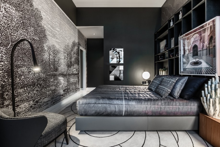 <span>Urbanitas Master Bedroom - Leo Shehtman. A suíte urbana enfatiza as diferenças: a paisagem do papel de parede tem personalidade e contrasta com azulejos cinza escuro, enquanto a contemporaneidade da cama em couro se contrapõe ao design mid-century do mobiliário. O tapete preto e branco está no centro de tudo e reforça a sobriedade do esquema de linhas e cores.</span>