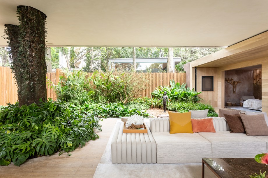 CASACOR São Paulo. Casa da Árvore Renault - Suite Arquitetos. O imenso flamboyant com costelas-de-adão na base rouba a cena. Sem barreiras físicas entre o living e o jardim, a integração com o verde é acentuada. Para prolongar o contato com o natural, foram eleitos tons terrosos nos revestimentos e nos móveis. Para finalizar, biombo em madeira, uma parede em mármore e a ilha gourmet em pedra. Daniela Frugiuele assina o projeto com Filipe Troncon e Carolina Mauro.