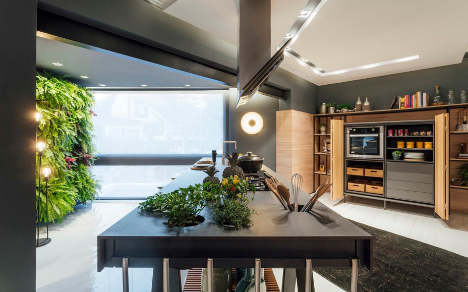 CASACOR Rio Grande do Sul. Atelier Culinário - W4 Arquitetura. A arte de cozinhar ganha um atelier à altura, que se desenvolve em torno da grande bancada. Ela é produzida em Dekton Kelya, com espaço para horta integrada e base ripada em lâminas de Carvalho natural. A marcenaria tem ares de armazém, com design de La Agencia, inspirada nas cozinhas de décadas passadas. A vegetação é farta, para trazer vida e frescor.