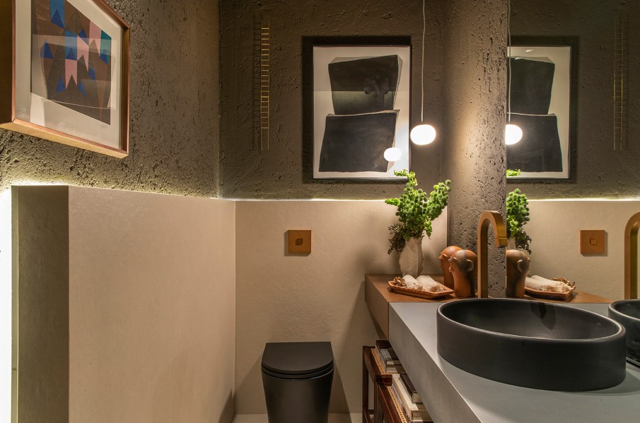 CASACOR Ribeirão Preto. Lavabo - Eduardo Franco Correia. O arquiteto proporciona uma imersão no universo natural com o uso de pedras, madeira e cimento rústico. A madeira de tonalidade capuccino cria uma interferência bem-vinda, no tampo em porcelanato de aspecto metálico. Nas paredes, o rústico ganha textura com o reboco sarrafeado artesanal e pintura no tom fendi, em diálogo com o porcelanato em placas de 1,20 x 1,20 m.