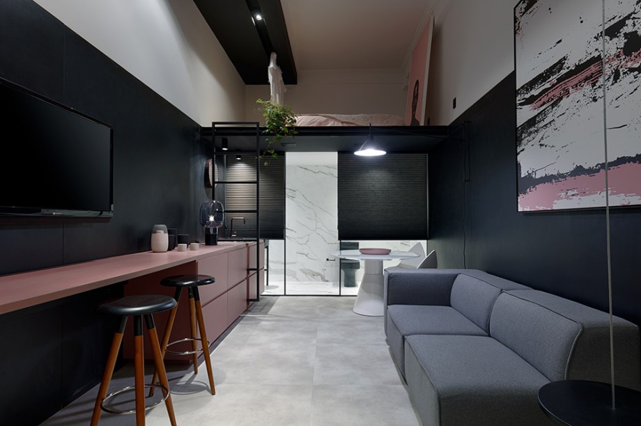 Loft Compacto do Jovem - por STUDIO SIMPLÍ (André França, Paula Freitas e Rute Zocrato). Preto, branco e rosa contrastam, destacando em primeiro plano algumas estratégias. Uma delas é a bancada que serve de apoio à área social e se estende até a cozinha, ao fundo. Discreta, a escada que desliza lateralmente leva ao mezanino, preservando a intimidade do quarto. Repare como a viga do ambiente foi utilizada como cabideiro e é por ela que corre a iluminação.