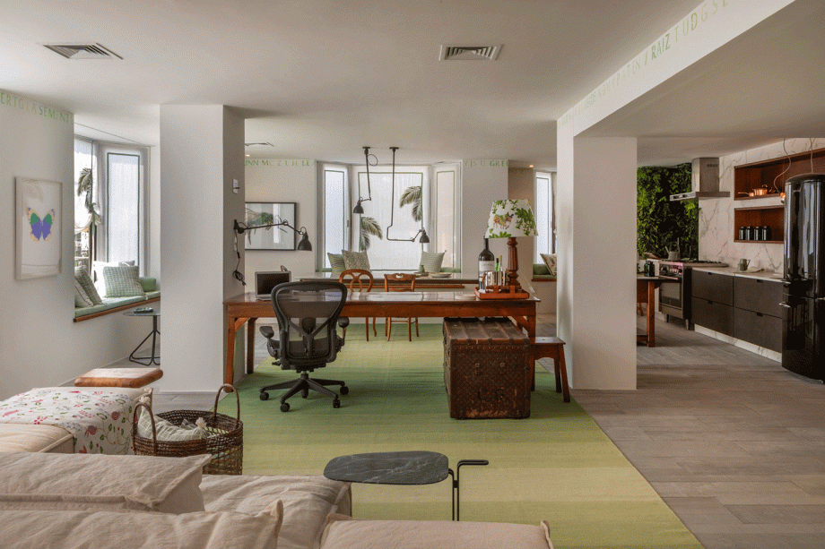 Sala Carioca - Marcia Müller e Manu Müller. O estilo de vida carioca e tropical chic inspirou o living multifuncional. Sobre o piso de tábuas de concreto, o tapete verde menta prolonga a visão e conecta espaços, da sala à copa, passando pelo escritório em direção á cozinha aberta. O sofá modulado permite experimentações de layout e convive com peças pontuais de época, como o baú. As bay-windows ganham almofadas e viram bancos.