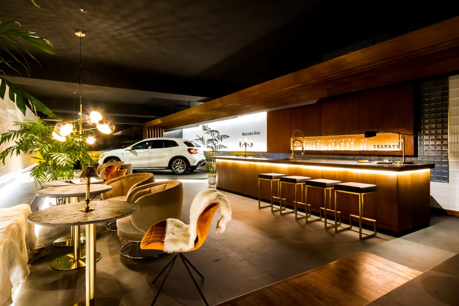 Mercedes-Benz Lounge By Aparici - Roberto Franco. A intervenção na garagem busca proporcionar uma experiência visual a partir do contraste de materiais. Alguns são muito nobres, segundo o arquiteto, como a madeira em estado natural. Ela contracena com a cerâmica Aparici que neutraliza o piso. Para arrematar, veludo nos móveis e detalhes metalizados.