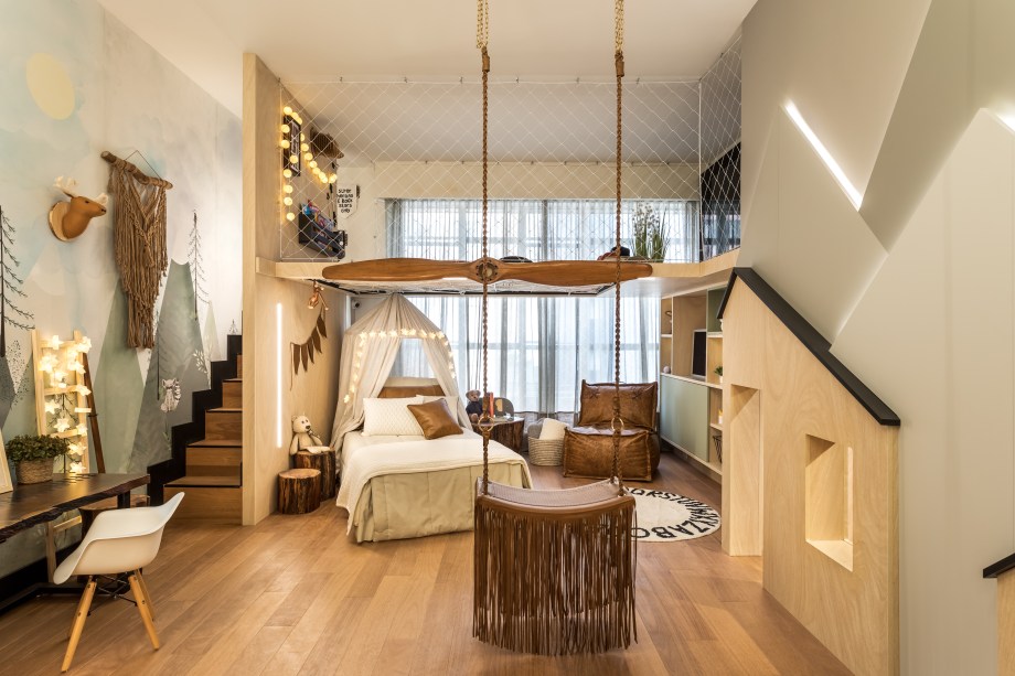 Suíte do Menino - Monica Pajewski e Renata Fraidg. O conceito escandinavo é a inspiração do espaço de 35 m², com móveis de linhas minimalistas e madeiras reaproveitadas empregadas na marcenaria. O grande destaque está na releitura da casa da árvore, no mezanino com rede no piso. Também há uma casa pensada para os pequenos e outra para um cãozinho, além de um balanço. Para completar a experiência lúdica, painel com montanhas.