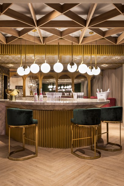 Bar e Espumanteria - Cynthia Karas. A arquitetura sensorial é explorada para instigar os sentidos, no ambiente de 116 m². O dourado marca presença nos revestimentos e nos detalhes, como a composição de pendentes de Michael Anastassiades para a Flos. A atmosfera é ainda mais sofiarticada com os espelhos emoldurados e o balcão em mármore, com banquetas estofadas em veludo. A madeira ganha destaque, redesenhando o forro.