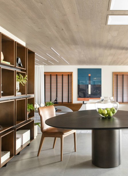 C4 Arquitetos - Living Perene. A madeira assume papel de destaque no teto, recortado por claraboias. Elas aproveitam a luz natural. assim como as generosas janelas de freijó. A mesa tem design de Arthur Casas.