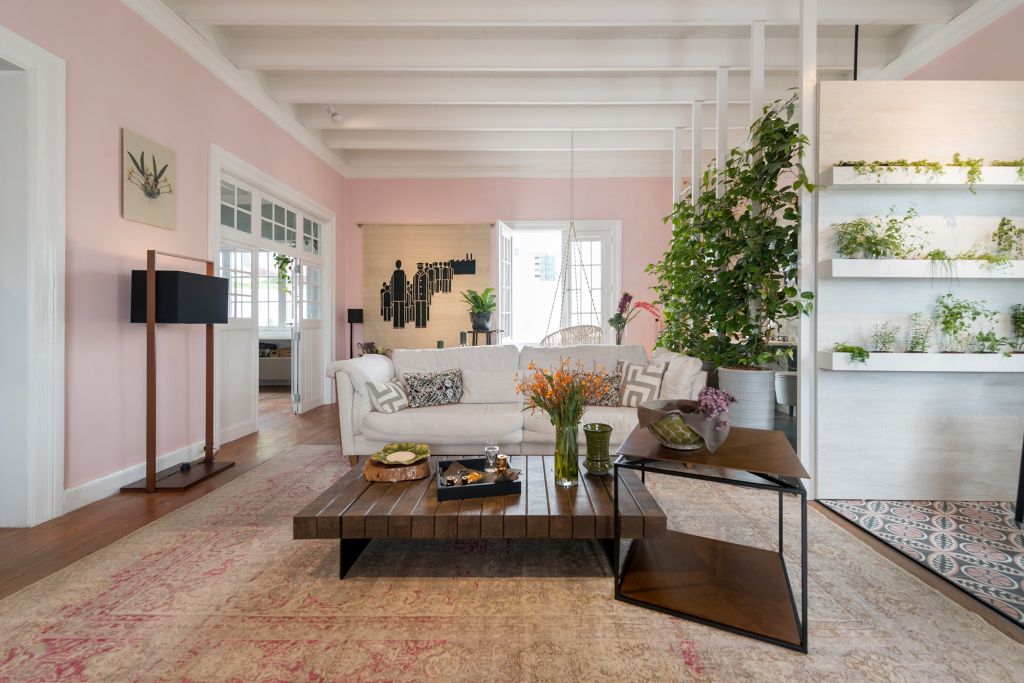 Loft com paredes rosas. Sofá branco no centro com mesa de apoio em madeira
