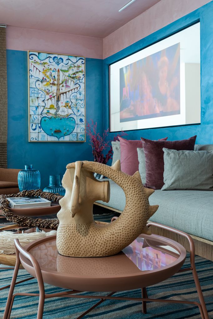 Foto vertical com escultura em primeiro plano, sofá e telão em segundo
