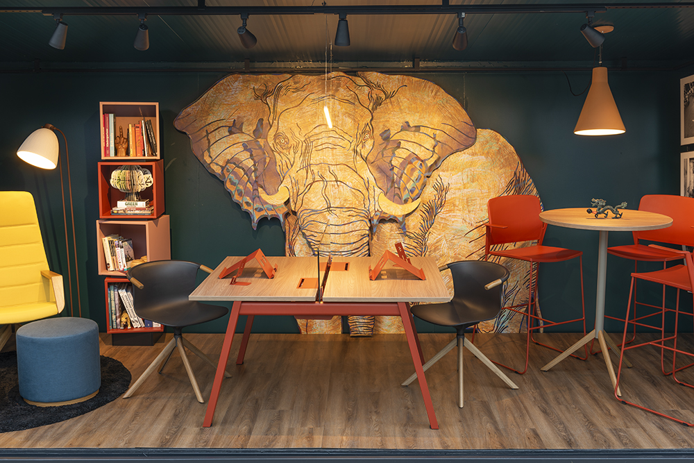 Vista frontal do co-working com mesa, duas cadeiras, uma estante à esquerda e na parede do centro um elefante grafitado