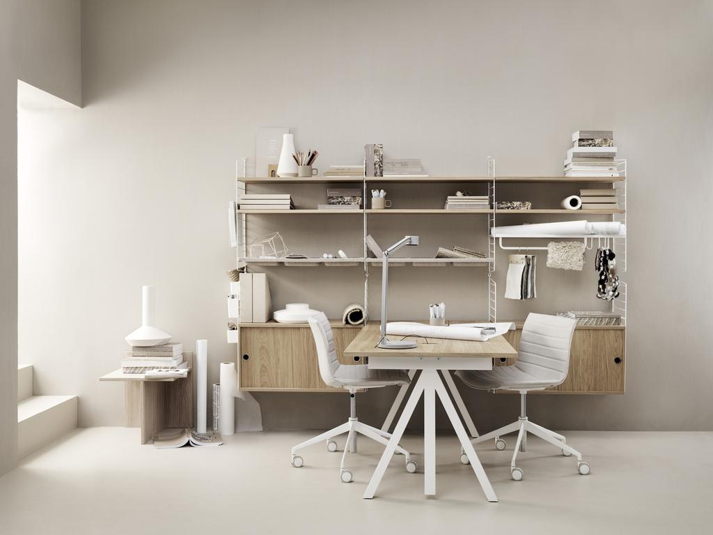 Escritório com prateleiras metálicas brancas e duas cadeiras de escritório brancas, uma de cada lado da mesa que se projeta em ângulo perpendicular das prateleiras