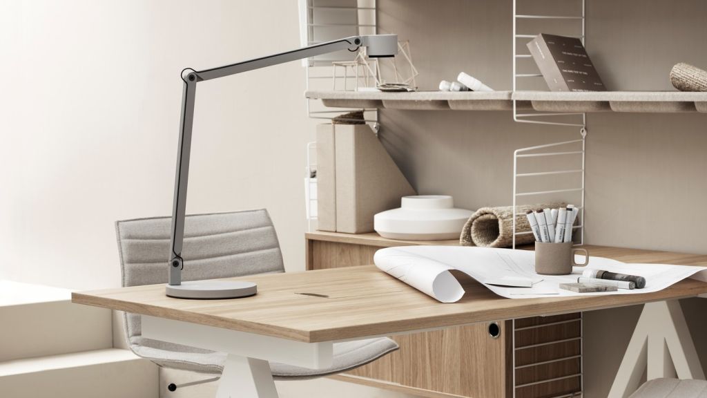 Mesa de escritório branca com tampo em madeira. Cadeira e luminária brancas. Prateleiras ao fundo