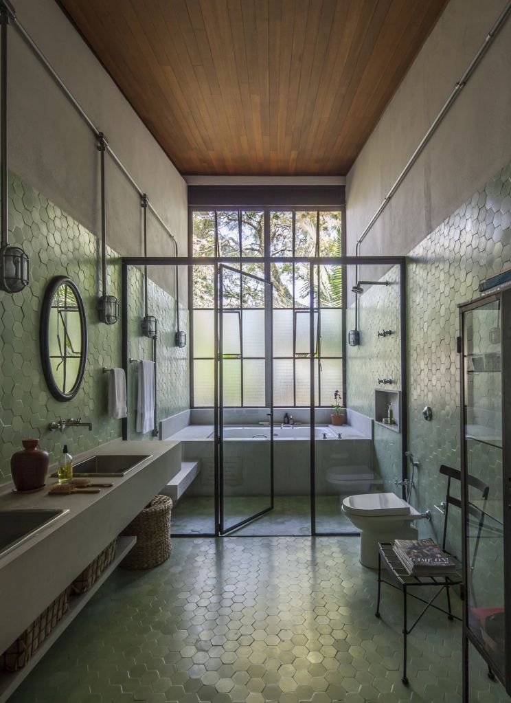 banheiro com revestimento verde na parede espelho e box transparente que abriga uma banheira
