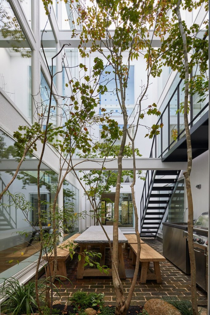 quintal no centro da residencia estilo mininalista pátio do projeto minimalista com vegetação e árvore no centro. Mesa de convívio para a família e churrasqueira também se encontram no local