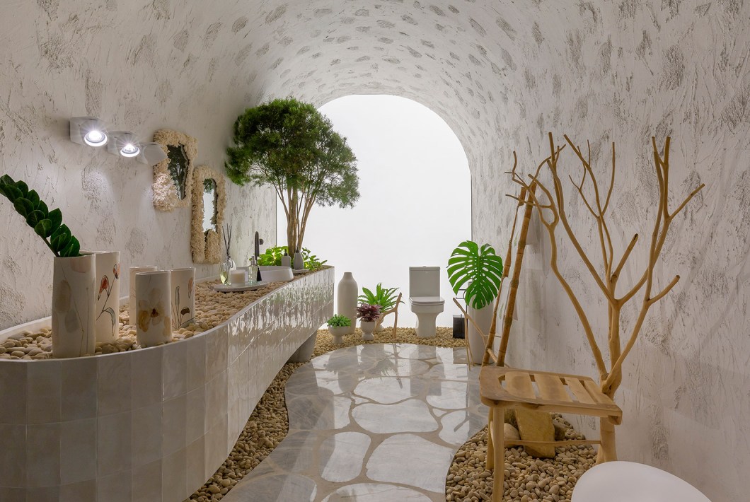 Paola Vasconcelos Albernaz e Lorrane Vasconcelos Albernaz - Lavabo Orgânico. Pensado para nos trazer à lembrança um passado histórico, este ambiente de 14 m² não possui pontas e nem retas. Inspirado na arquitetura rupestre, o arco remete ao interior de uma caverna e a tela iluminada representa a saída. As paredes mal-acabadas e a composição de retalhos de pedras no piso ajudam a compor a sensação de se estar dentro de uma gruta. A sofisticação do espaço é entregue pela luminária de piso assinada pelo designer Jader Almeida. Paola Vasconcelos Albernaz e Lorrane Vasconcelos Albernaz - Lavabo Orgânico. Pensado para nos trazer à lembrança um passado histórico, este ambiente de 14 m² não possui pontas e nem retas. Inspirado na arquitetura rupestre, o arco remete ao interior de uma caverna e a tela iluminada representa a saída. As paredes mal-acabadas e a composição de retalhos de pedras no piso ajudam a compor a sensação de se estar dentro de uma gruta. A sofisticação do espaço é entregue pela luminária de piso assinada pelo designer Jader Almeida.