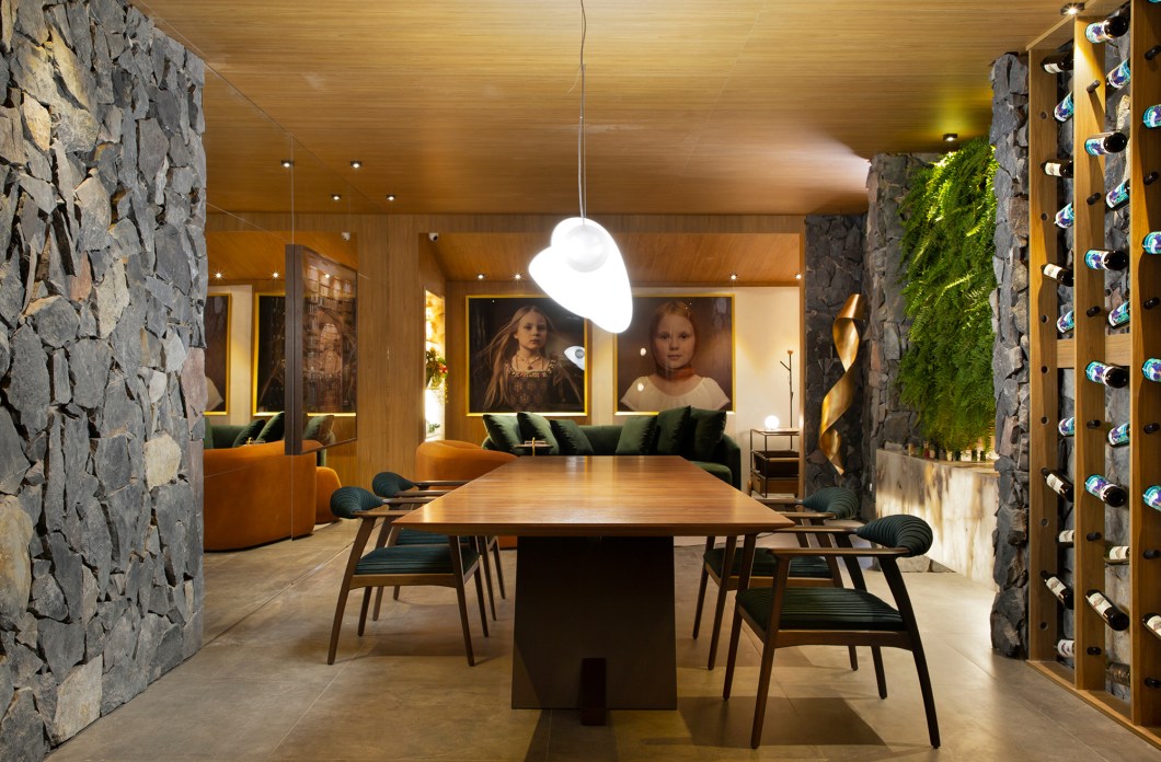 Janaína Dias - Sala do Colecionador. A busca pelo acolhimento é a essência dos projetos da arquiteta Janaína Dias, conceito que ela buscou ao criar este espaço multifuncional que tem como ponto de partida uma ampla mesa de jantar. A funcionalidade ganha destaque no bar com adega e champanheira esculpida em mármore. O sofá convida a momentos de relaxamento e confraternização e paredes revestidas de pedras naturais abrigam o jardim vertical garantindo aconchego. Telas são expostas em meio aos elementos naturais. Janaína Dias - Sala do Colecionador. A busca pelo acolhimento é a essência dos projetos da arquiteta Janaína Dias, conceito que ela buscou ao criar este espaço multifuncional que tem como ponto de partida uma ampla mesa de jantar. A funcionalidade ganha destaque no bar com adega e champanheira esculpida em mármore. O sofá convida a momentos de relaxamento e confraternização e paredes revestidas de pedras naturais abrigam o jardim vertical garantindo aconchego. Telas são expostas em meio aos elementos naturais.