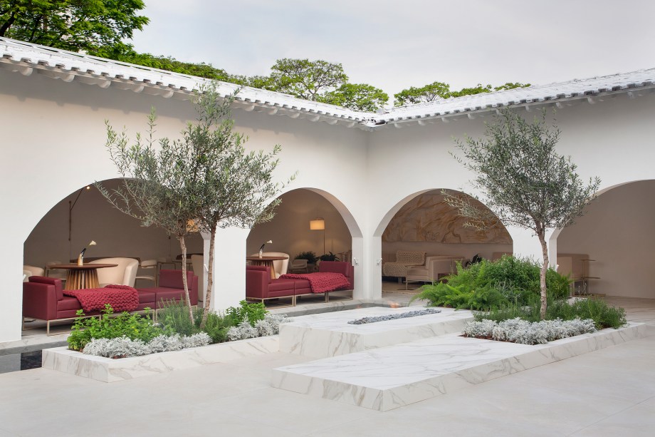 Deborah Nazareth e Gisele Viana - Átrio Bodoquena. Os arcos originais da casa abraçam a praça integrada ao restaurante, o paisagismo cria sensações por meio de ervas aromáticas como alecrim, hortelã e manjericão, que exalam aromas. Oliveiras, romã e lavandas trazem a essência do mediterrâneo; e a Costela de Adão e a Guaimbê, tropicalismo. Monolitos, da Serra de Bodoquena, com suas formas orgânicas são um belo contraste com a arquitetura de linhas retas. O espelho d’água pode ser atravessado por outro monolito. Nele, seixos rolados lembram o leito de um rio, enquanto uma cascata garante tranquilidade e ajuda a refrescar o ambiente.