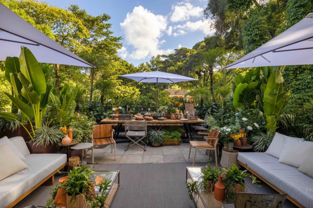 Anna Luiza Rothier - Muito Além do Jardim. Um recanto a céu aberto, ligeiramente protegido da chuva por ombrelones, e com espaço de sobra para encontros informais e descontraídos, que são a cara do Rio. Com vista para os jardins e para (quase) tudo o que acontece na área externa da casa, o terraço se insere ainda mais na paisagem natural do entorno pelo uso de diversas espécies de plantas e pelo jardim vertical, que toma toda a parede principal. Um ambiente tropical, leve, despretensioso e bem carioca.