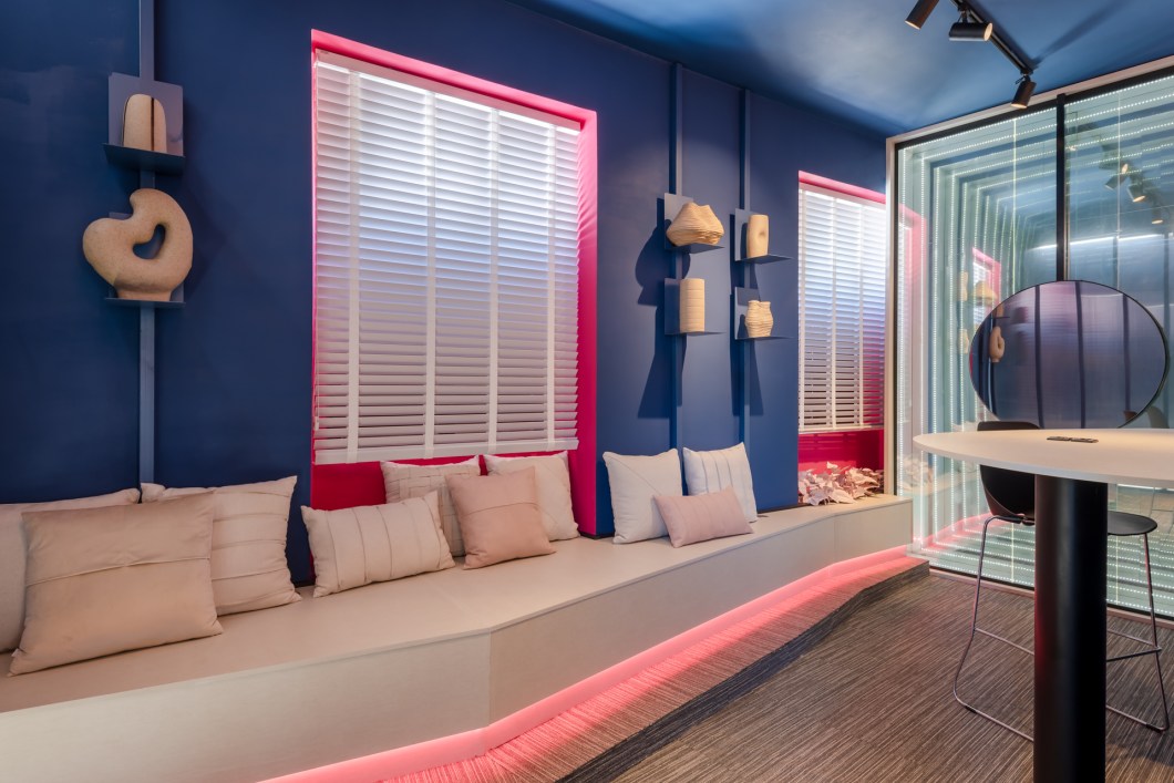 Studio Noventa - Design Lab. Todo o ambiente projetado pelo escritório de arquitetura Studio Noventa tem um “ar de surpresa”. Em apenas 14 m², abre-se um espaço que visa estabelecer conexões, fomentar negócios e que apresenta novas possibilidades. As cores escolhidas evocam uma atmosfera sóbria, digital e, junto com a iluminação, apresentam um ambiente de inovação e tecnologia, que ainda conta com um grande banco, permitindo ao visitante uma pausa no percurso. O Design LAB é um espaço híbrido, que equilibra a pausa e o movimento. A pausa está no espelho infinito, que reflete ao visitante suas próprias oportunidades: infinitas. O movimento, por sua vez, se encontra na necessidade de se expressar, de unir a sobriedade de um espaço corporativo com o “ser disruptivo” de um mercado tecnológico cada vez mais orgânico. Esse movimento está na paleta de cores, azul profundo e magenta, e nas formas livres dos objetos. Studio Noventa - Design Lab. Todo o ambiente projetado pelo escritório de arquitetura Studio Noventa tem um “ar de surpresa”. Em apenas 14 m², abre-se um espaço que visa estabelecer conexões, fomentar negócios e que apresenta novas possibilidades. As cores escolhidas evocam uma atmosfera sóbria, digital e, junto com a iluminação, apresentam um ambiente de inovação e tecnologia, que ainda conta com um grande banco, permitindo ao visitante uma pausa no percurso. O Design LAB é um espaço híbrido, que equilibra a pausa e o movimento. A pausa está no espelho infinito, que reflete ao visitante suas próprias oportunidades: infinitas. O movimento, por sua vez, se encontra na necessidade de se expressar, de unir a sobriedade de um espaço corporativo com o “ser disruptivo” de um mercado tecnológico cada vez mais orgânico. Esse movimento está na paleta de cores, azul profundo e magenta, e nas formas livres dos objetos.