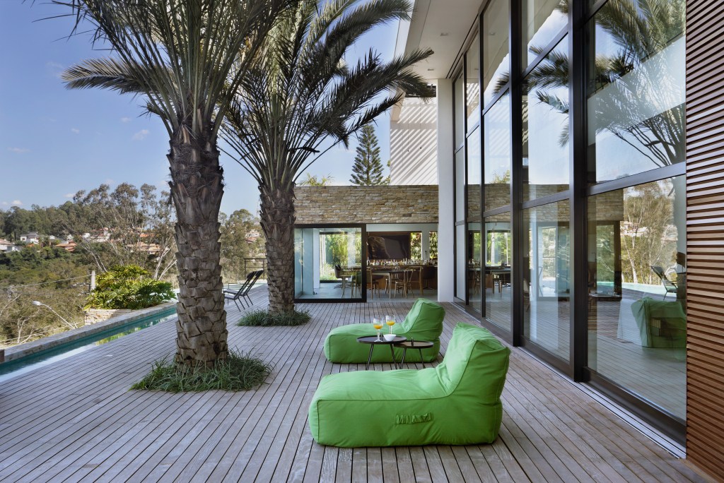 Parede pedra integra interno externo casa de campo. Otto Felix arquitetura decoração paisagismo jardim piscina deque madeira cadeira varanda