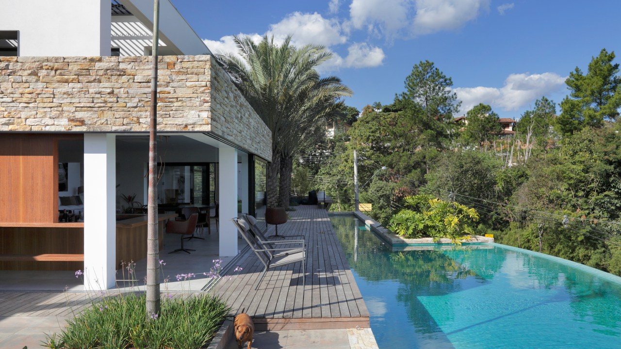 Parede pedra integra interno externo casa de campo. Otto Felix arquitetura decoração paisagismo jardim piscina deque madeira cadeira varanda