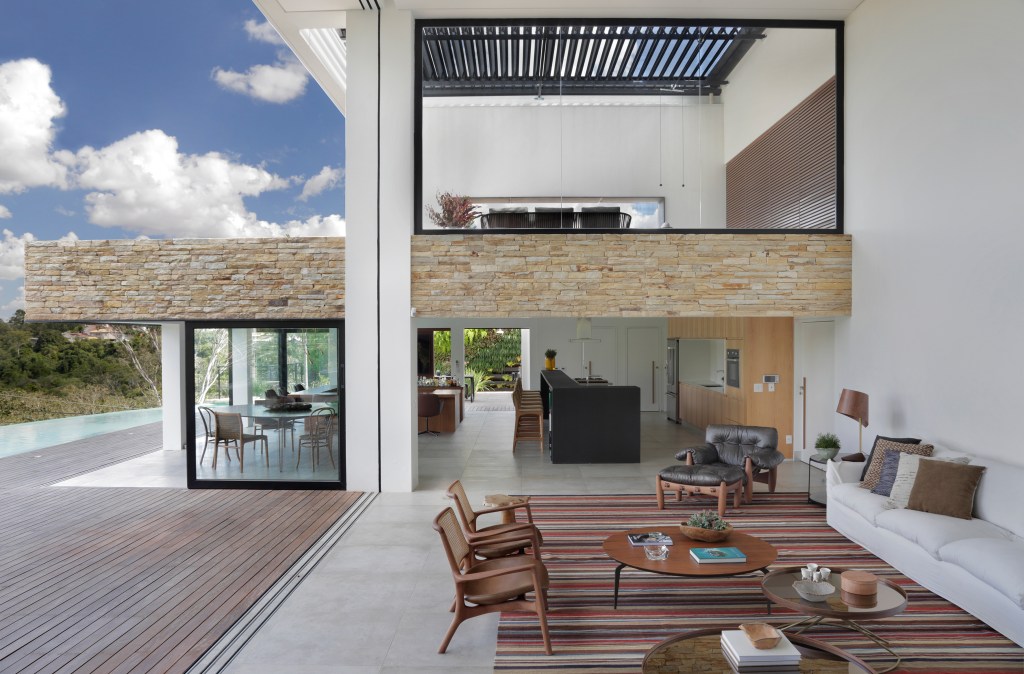 Parede pedra integra interno externo casa de campo. Otto Felix arquitetura decoração sala vidro deque madeira estar cozinha