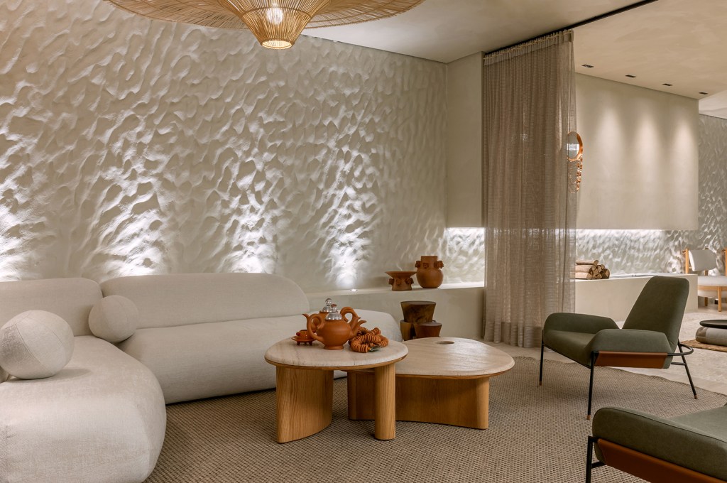 Mariana Mendonça - Remanso. Projeto da CASACOR Goiás 2023. Na foto, sala de estar com parede texturizada, sofá curvilíneo e luminária de fibra.