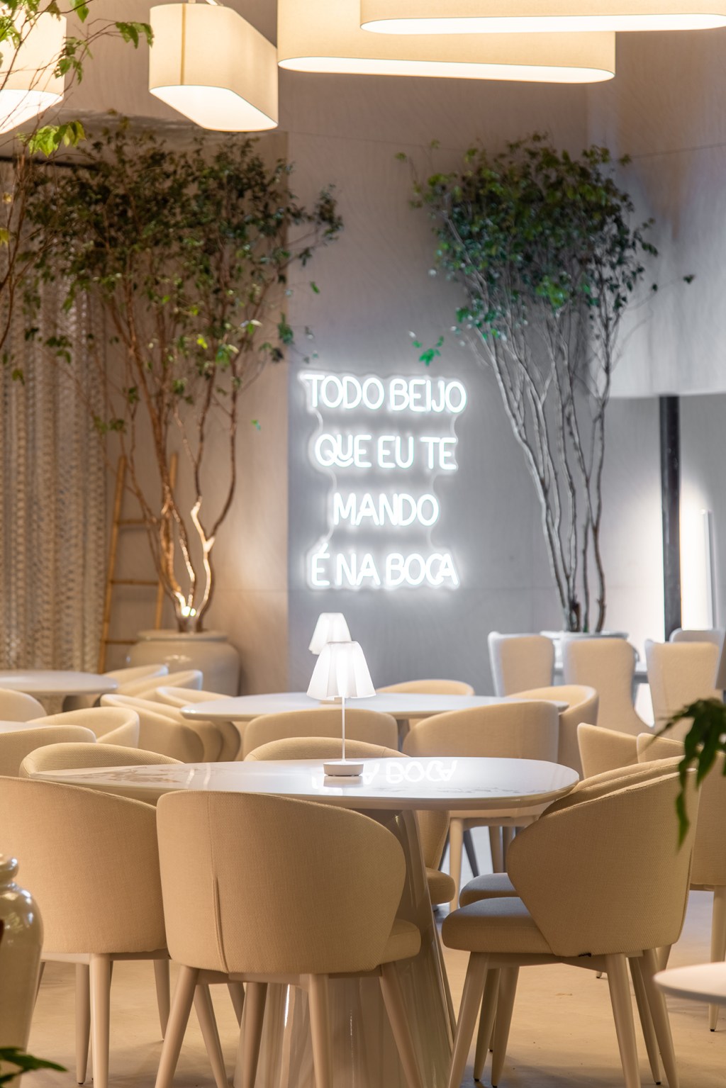 Carla Felippi - Casa em Mykonos | MYK. Projeto da CASACOR São Paulo 2023. NA foto, restaurante com mesa, cadeira,, plantas e neon.
