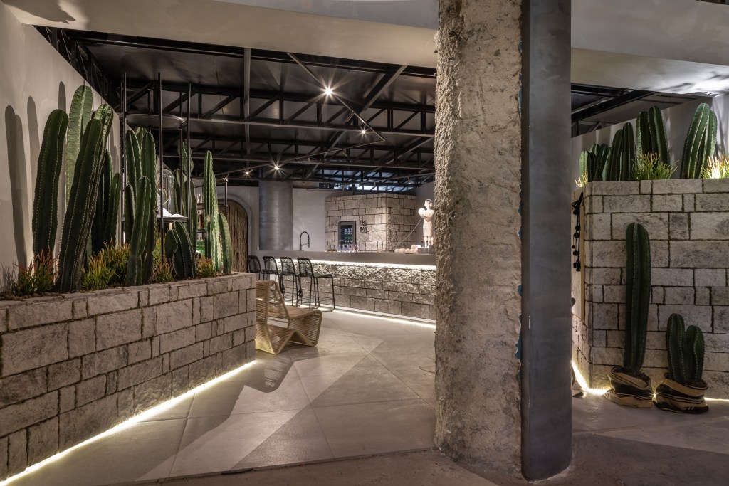 Eduardo Baldelomar - UYUNI Lounge The - Bar. Projeto da CASACOR São Paulo 2023. Na foto, paredes de pedra, jardim de cacots e pilar rústico.