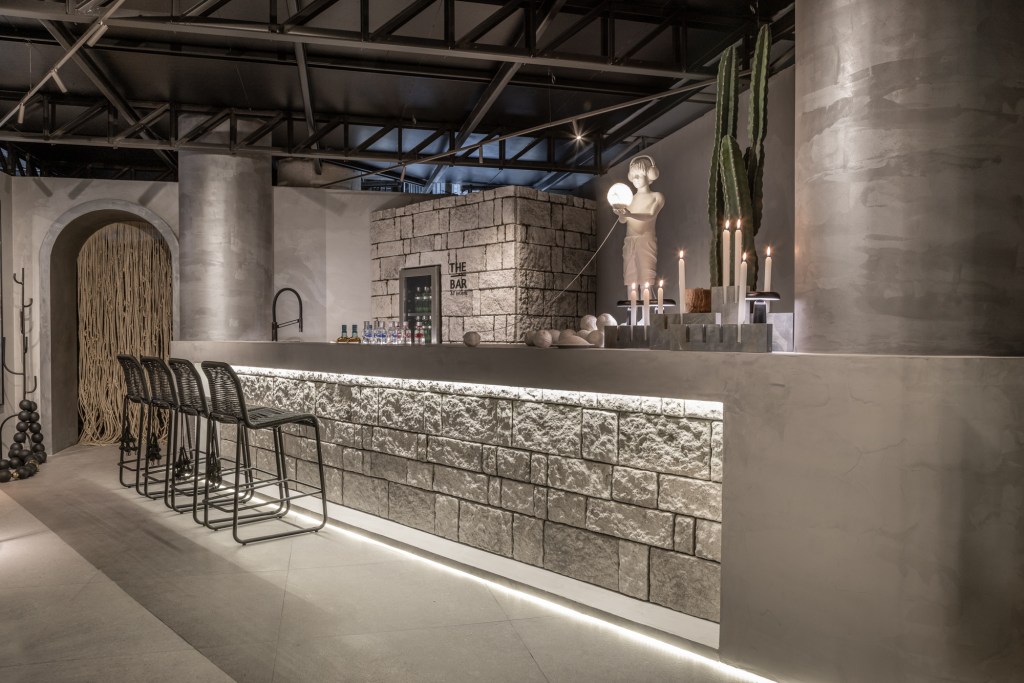 Eduardo Baldelomar - UYUNI Lounge The - Bar. Projeto da CASACOR São Paulo 2023. Na foto, bar com balcão de pedra iluminado e velas.