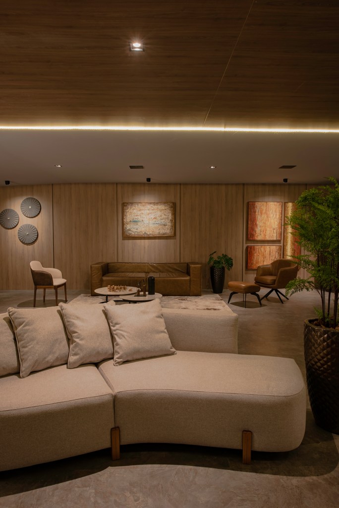Mapogos Design - Lounge Oasis. Projeto da CASACOR Paraná 2023. Na foto, sala com parede de madeira, sofa de couro e quadros.