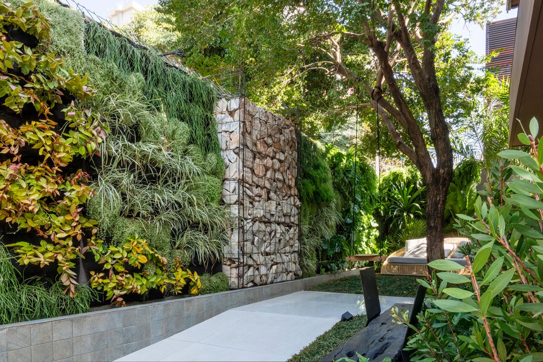 Victor Thauan - Refúgio do Mato. O jardim é um convite à paz e à tranquilidade, proporcionados pela fusão de elementos naturais, como o fogo, folhagens, pedra e água. O protagonismo da parede de pedra e do elemento água criam uma conexão de leveza com o verde presente nas plantas e também com a presença do fogo. A proposta do paisagista foi de conectar o ser humano com a natureza, contribuindo para promover a qualidade de vida e a saúde daqueles que se permitem a experiência de desfrutar desses pequenos oásis em meio aos caos. Victor Thauan - Refúgio do Mato. O jardim é um convite à paz e à tranquilidade, proporcionados pela fusão de elementos naturais, como o fogo, folhagens, pedra e água. O protagonismo da parede de pedra e do elemento água criam uma conexão de leveza com o verde presente nas plantas e também com a presença do fogo. A proposta do paisagista foi de conectar o ser humano com a natureza, contribuindo para promover a qualidade de vida e a saúde daqueles que se permitem a experiência de desfrutar desses pequenos oásis em meio aos caos.