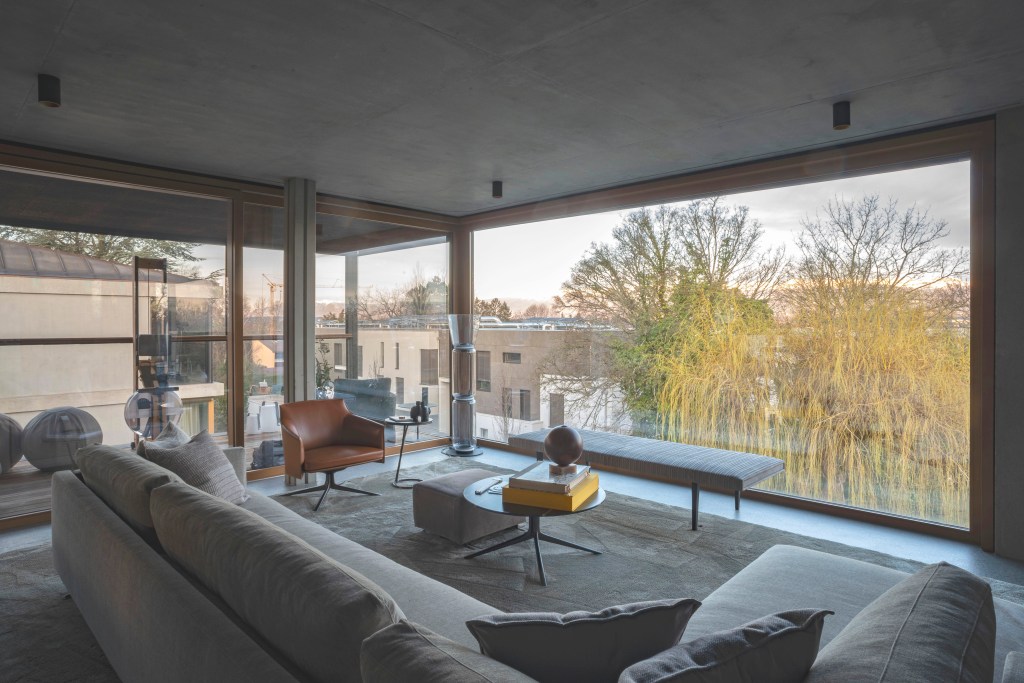 David Bastos projeta apartamento na Suíça repleto de design assinado. Na foto, sala de estar com parede de vidro, sofa e banco.