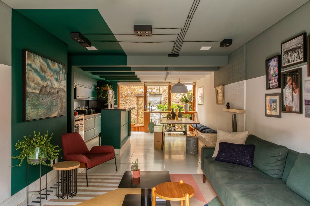Degradê de tons de verde setoriza esta casa de vila em São Paulo. Projeto de Ricardo Abreu. Na foto, sala e cozinha com paredes verdes, sofá e quadros.