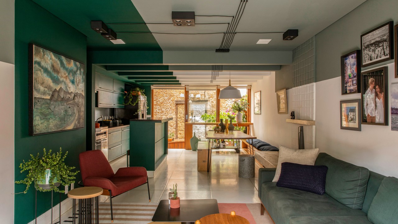 Degradê de tons de verde setoriza esta casa de vila em São Paulo. Projeto de Ricardo Abreu. Na foto, sala e cozinha com paredes verdes, sofá e quadros.