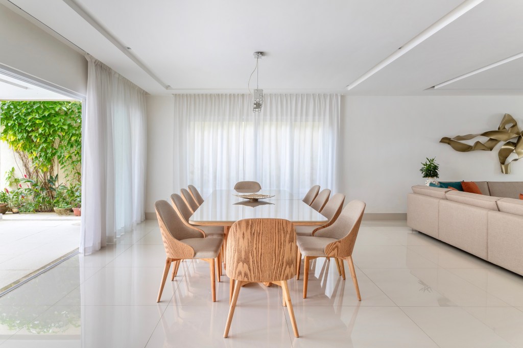 Janelas até o teto emolduram a natureza nesta sala de 200 m². Projeto de Ana Cano Milman. Na foto, sala de jantar com varanda, cortinas e cadeiras de madeira.