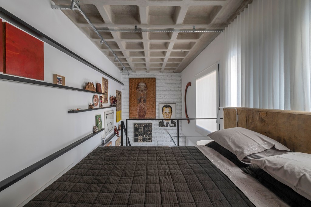 Loft de 64 m² ganha décor industrial e coleção de arte dos moradores. Projeto de Junior Piacesi. Quarto com quadros, laje nervurada e serralheria.