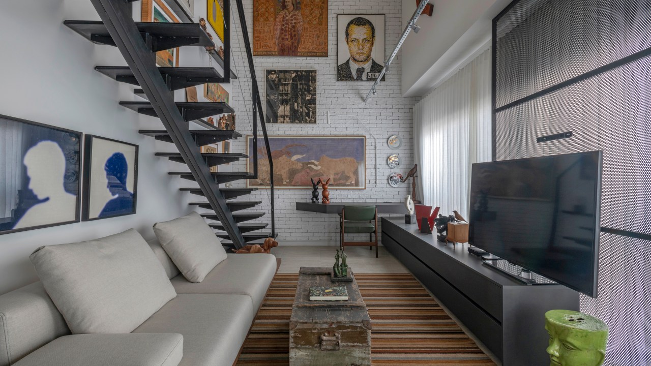 Loft de 64 m² ganha décor industrial e coleção de arte dos moradores. Projeto de Junior Piacesi. Na foto, escada com gallery wall na parede. Sala de estar com tapete listrado.