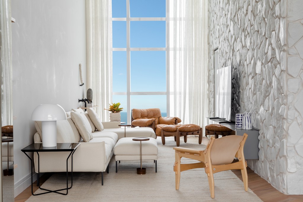 Tufi Mousse assina apê no 46º andar com vista para o mar catarinense. Na foto, sala com sofá branco e parede de pedra.