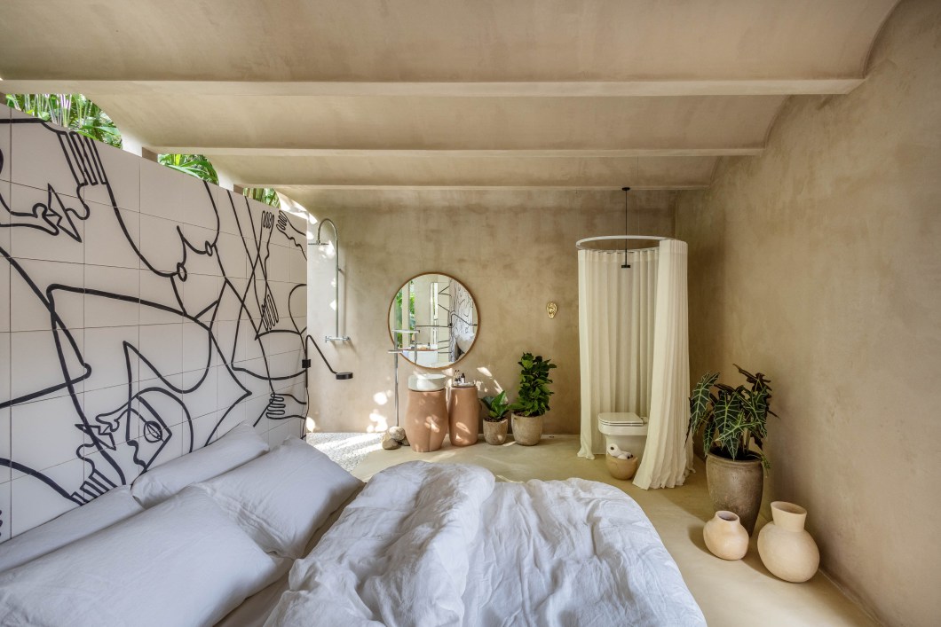 Bric Arquitetura - Mariana Teixeira e Pedro Pantoja - Palacito Bric. Pensada como uma extensão do corpo, a suíte de Mariana Teixeira e Pedro Pantoja foi totalmente revestida de cimento em tom que remete à pele. Erguida como um volume monolítico, é camuflada pela vegetação – que invade o interior na área da banheira. O desenho da arquitetura, com arcos inspirados no Palácio do Itamaraty, conduz o olhar pelo ambiente que traz apenas o essencial no mobiliário. Um painel de azulejos da artista espanhola Noemi Carpu faz a divisão entre cama e banheira e traz mais uma vez as curvas do corpo humano, que aparecem também nas belas cubas de cerâmica do banheiro. Bric Arquitetura - Mariana Teixeira e Pedro Pantoja - Palacito Bric. Pensada como uma extensão do corpo, a suíte de Mariana Teixeira e Pedro Pantoja foi totalmente revestida de cimento em tom que remete à pele. Erguida como um volume monolítico, é camuflada pela vegetação – que invade o interior na área da banheira. O desenho da arquitetura, com arcos inspirados no Palácio do Itamaraty, conduz o olhar pelo ambiente que traz apenas o essencial no mobiliário. Um painel de azulejos da artista espanhola Noemi Carpu faz a divisão entre cama e banheira e traz mais uma vez as curvas do corpo humano, que aparecem também nas belas cubas de cerâmica do banheiro.