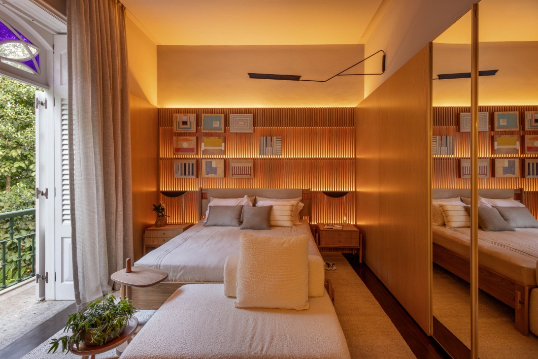 STUDIO 021 - Quarto 021. Um dos quartos originais da Residência Brando Barbosa ganha novos ares com a intervenção das arquitetas Camila Simbalista e Paula Wetzel. A dupla aproveitou muitas das características originais do ambiente, como pé-direito alto, esquadrias generosas e piso de madeira maciça, mas criou um projeto contemporâneo com peças de design nacional assinado e painéis de carvalho natural que revestem praticamente todo o espaço. A paleta de cores neutras, a iluminação indireta e o uso de diferentes texturas trazem aconchego e um clima de quarto residencial, que convida à permanência. STUDIO 021 - Quarto 021. Um dos quartos originais da Residência Brando Barbosa ganha novos ares com a intervenção das arquitetas Camila Simbalista e Paula Wetzel. A dupla aproveitou muitas das características originais do ambiente, como pé-direito alto, esquadrias generosas e piso de madeira maciça, mas criou um projeto contemporâneo com peças de design nacional assinado e painéis de carvalho natural que revestem praticamente todo o espaço. A paleta de cores neutras, a iluminação indireta e o uso de diferentes texturas trazem aconchego e um clima de quarto residencial, que convida à permanência.