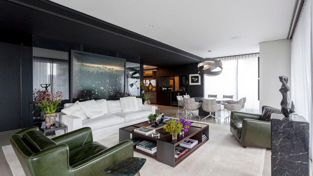 David Bastos assina apê de 268 m² com décor sóbrio e elegante. Na foto, sala de estar com poltrona preta, sofá branco e jantar integrado.