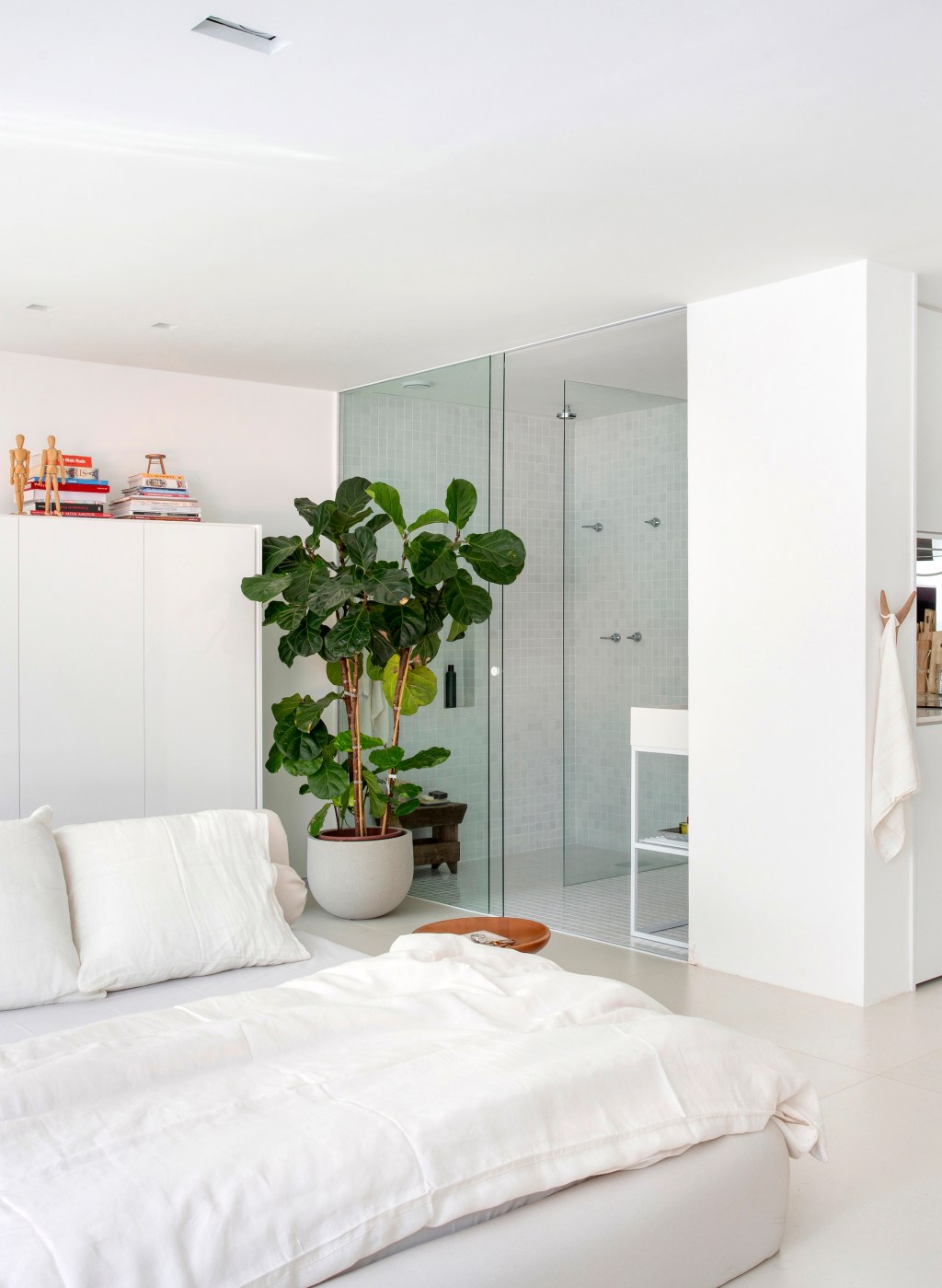 loft-40-m2-projeto-minimalista-une-branco-madeira-diego-raposo-manuela-simas-credito-mca (10) Loft de 40 m² ganha projeto minimalista que une branco e madeira. Projeto de Diego Raposo e Manuela Simas. Na foto quarto com banheiro integrado. Vaso de plantas e cama.
