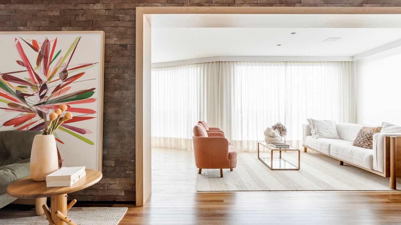 Parede de tijolos e painéis de madeira trazem acolhimento ao apê de 310 m². Projeto Très Arquitetura. Na foto, sala de estar com parede de tijolinhos e madeira e varanda integrada.