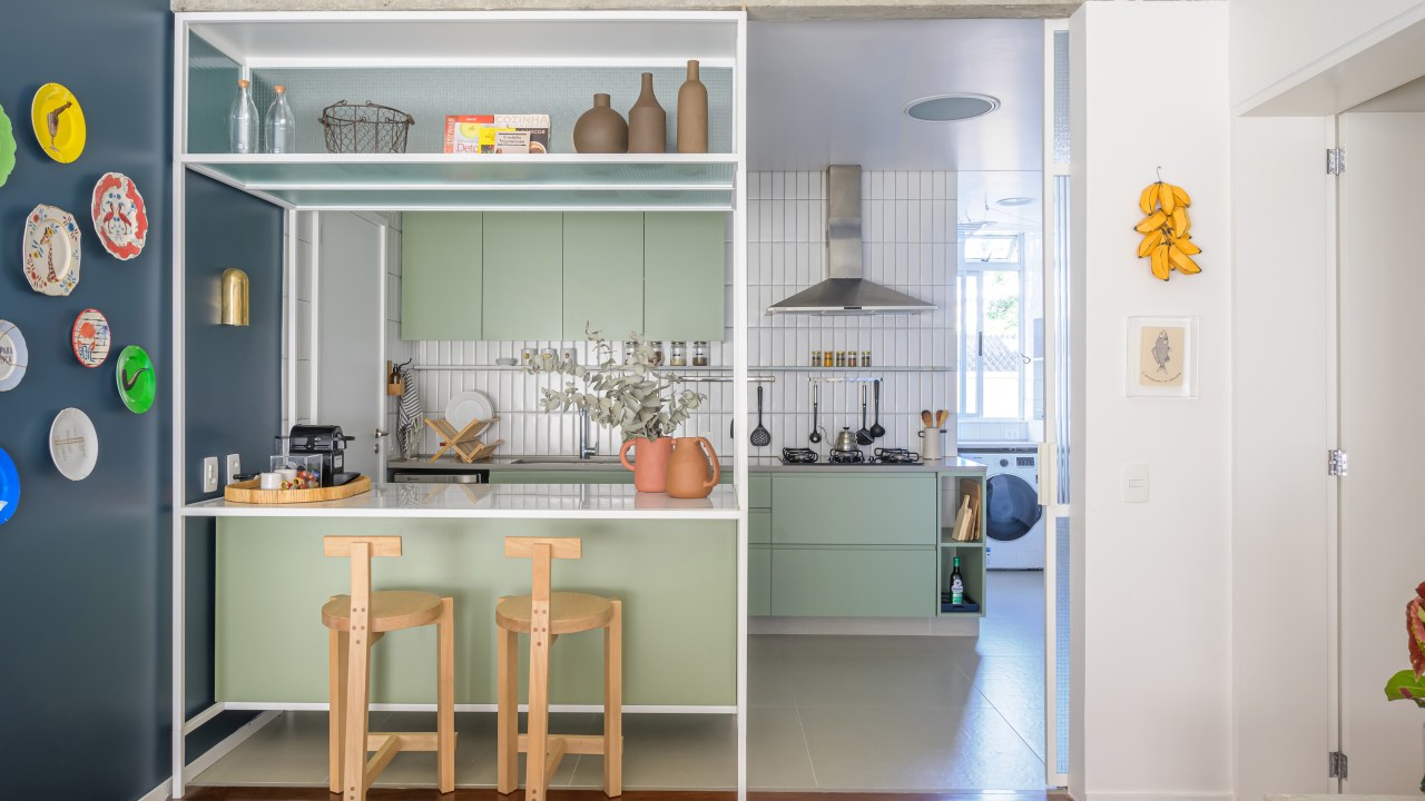 Pilar estrutural e tijolos aparentes dão o tom deste apê de 115 m². Projeto de Ana Neri. Na foto, cozinha integrada com a sala, móvel de serralheria e parede azul com quadros.