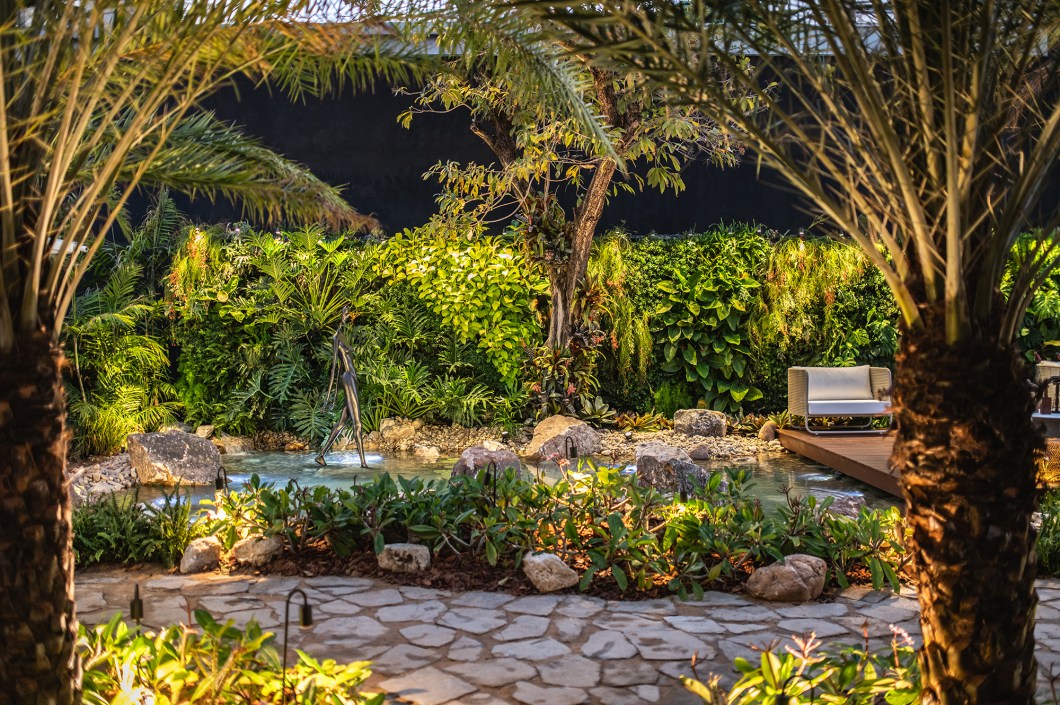 Droysen Tomich e Gerson Munayer - Jardim dos Encontros e Despedidas. <span>Explorando a simbiose entre o ser humano e a natureza, residências com jardins em fusão contemplativa e funcional emergem como catalisadoras do bem-estar integral. No coração da mostra, o jardim se revela como um oásis versátil, convidando os visitantes a uma imersão sensorial. A sinfonia da água caindo em um sereno lago induz a um relaxamento profundo, enquanto espécies tropicais adaptadas ao clima local e uma vibrante parede viva se fundem em um balé de texturas e cores. O mobiliário em branco off white e uma escultura imponente conferem elegância e leveza. Um espaço que explora o elo vital entre o ser humano e o ambiente que o circunda. </span> Droysen Tomich e Gerson Munayer - Jardim dos Encontros e Despedidas. <span>Explorando a simbiose entre o ser humano e a natureza, residências com jardins em fusão contemplativa e funcional emergem como catalisadoras do bem-estar integral. No coração da mostra, o jardim se revela como um oásis versátil, convidando os visitantes a uma imersão sensorial. A sinfonia da água caindo em um sereno lago induz a um relaxamento profundo, enquanto espécies tropicais adaptadas ao clima local e uma vibrante parede viva se fundem em um balé de texturas e cores. O mobiliário em branco off white e uma escultura imponente conferem elegância e leveza. Um espaço que explora o elo vital entre o ser humano e o ambiente que o circunda. </span>